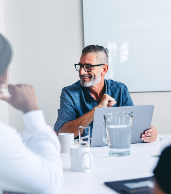 Mature supervisor having a meeting with his colleagues in an office. Experienced businessman smiling while briefing his team in a meeting room. Group of creative businesspeople working together.