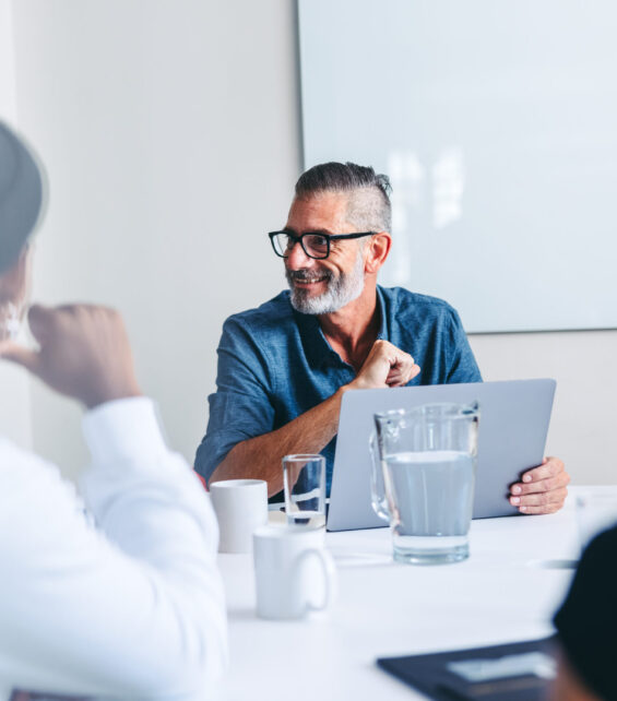 Mature supervisor having a meeting with his team in an office Mature supervisor having a meeting with his colleagues in an office. Experienced businessman smiling while briefing his team in a meeting room. Group of creative businesspeople working together.